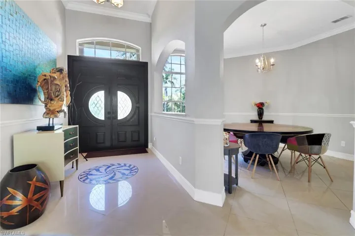 Foyer with crown molding, a chandelier, arched walkways, and tile patterned flooring