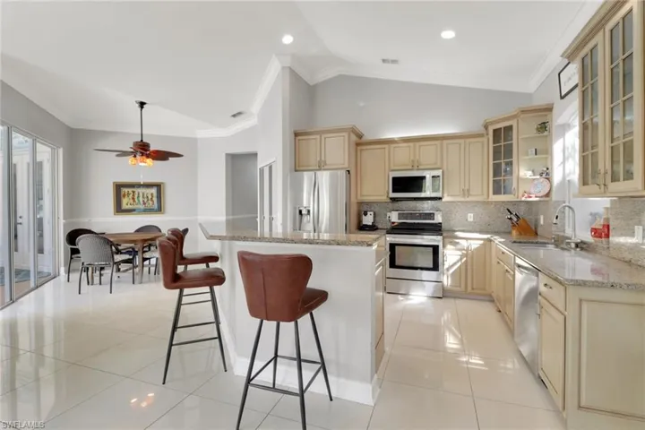 Kitchen with crown molding, glass insert cabinets, appliances with stainless steel finishes, light stone counters, and a kitchen island