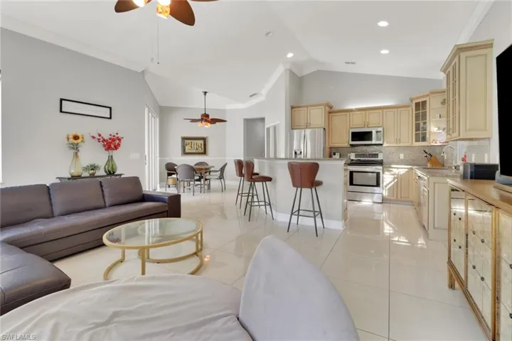 Living room with ceiling fan, crown molding, light tile patterned flooring, and high vaulted ceiling