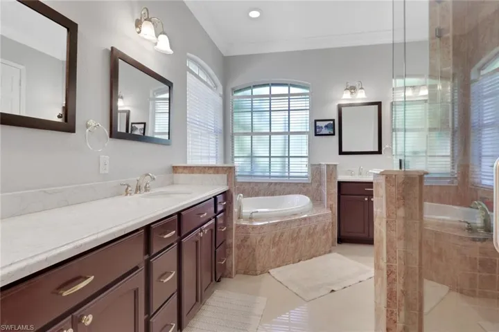 Bathroom featuring two vanities, a garden tub, a shower stall, crown molding, and light tile patterned floors
