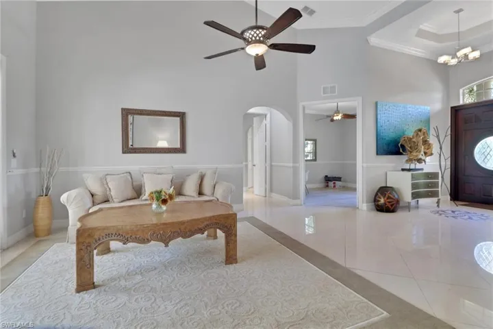 Living room featuring a towering ceiling, arched walkways, tile patterned flooring, ceiling fan, and ornamental molding