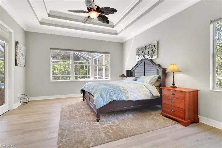 Bedroom featuring a raised ceiling, access to outside, multiple windows, light wood finished floors, and ornamental molding