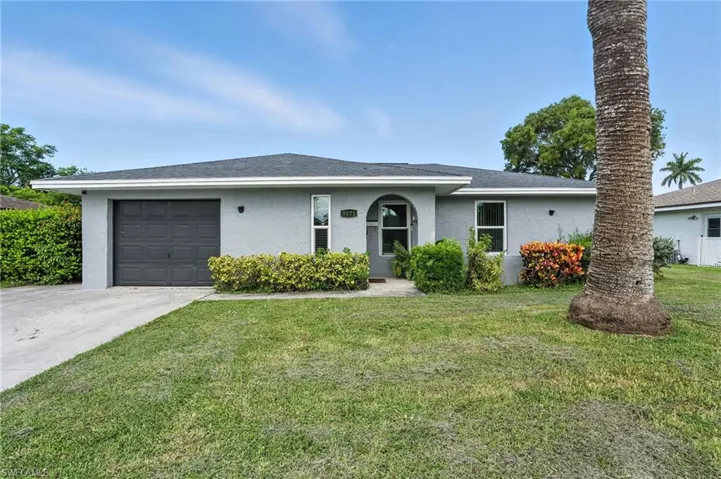 Ranch-style house featuring stucco siding, a front lawn, driveway, and a garage