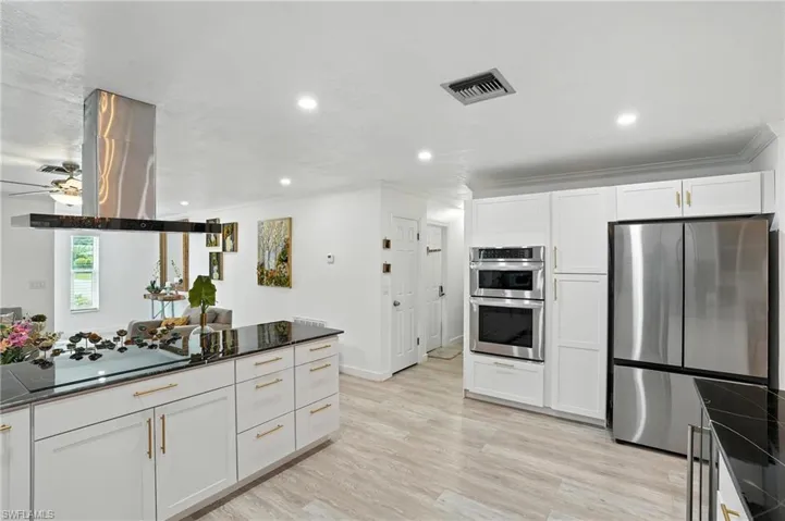 Kitchen featuring stainless steel appliances, white cabinets, island range hood, dark stone counters, and ornamental molding