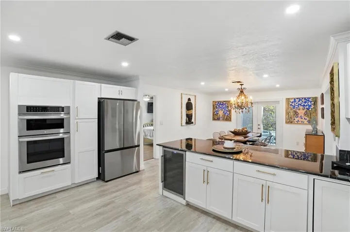 Kitchen with dark stone counters, white cabinetry, appliances with stainless steel finishes, decorative light fixtures, and beverage cooler