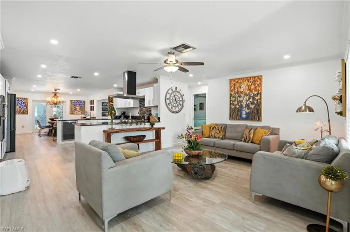 Living room with a chandelier, light wood-style floors, recessed lighting, ornamental molding, and beverage cooler