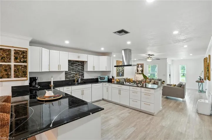 Kitchen with a peninsula, white cabinets, open floor plan, tasteful backsplash, and island exhaust hood