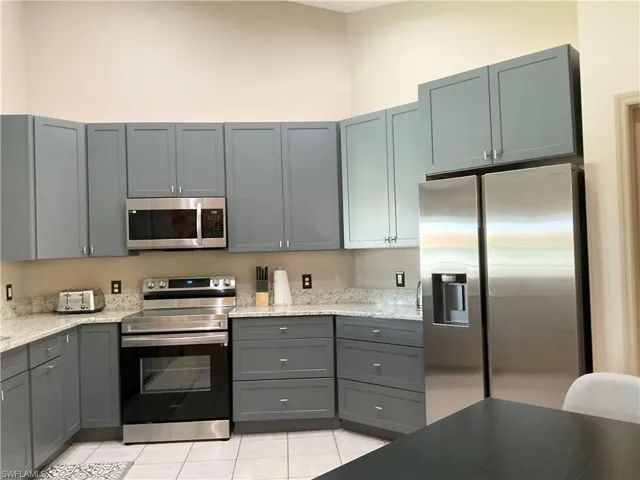 Kitchen with light stone countertops, light tile patterned floors, appliances with stainless steel finishes, and gray cabinets