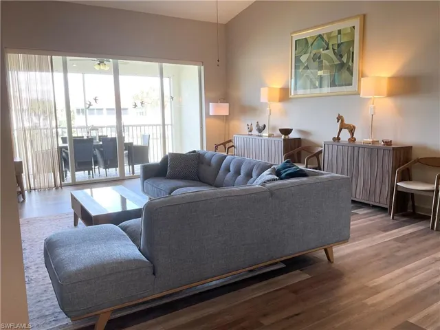 Living room with laminate wood-style floors, ceiling fan, and vaulted ceiling. Slider open to screened-in lanai