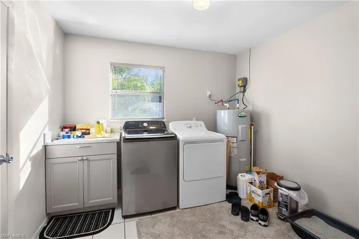 Laundry room with electric water heater, light tile patterned floors, and separate washer and dryer