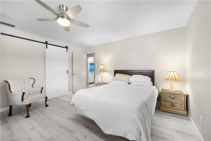 Bedroom featuring a barn door, ceiling fan, and light wood-style flooring