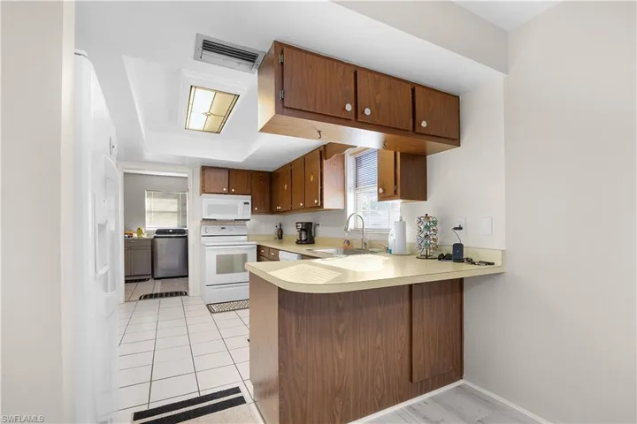 Kitchen featuring a peninsula, light countertops, white appliances, washer / clothes dryer, and brown cabinetry