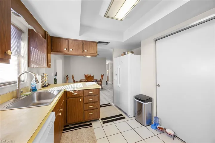 Kitchen with a peninsula, a tray ceiling, white appliances, light countertops, and brown cabinets