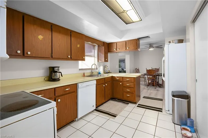 Kitchen featuring white appliances, brown cabinetry, a peninsula, light tile patterned flooring, and light countertops