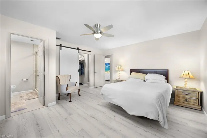 Bedroom with ensuite bathroom, a barn door, a spacious closet, and light wood-style flooring
