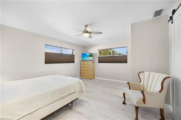 Bedroom featuring a barn door, light wood-style flooring, and ceiling fan