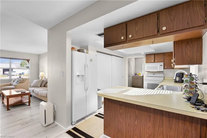 Kitchen with white appliances, light countertops, a peninsula, open floor plan, and brown cabinets