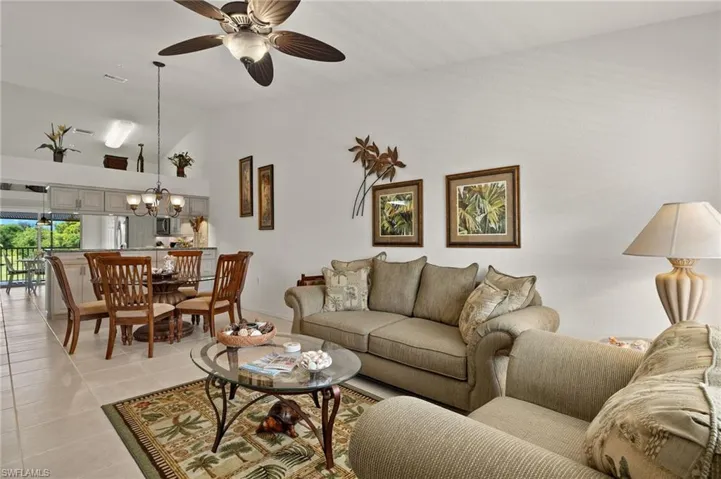 Living room featuring ceiling fan with notable chandelier, high vaulted ceiling, and light tile patterned flooring
