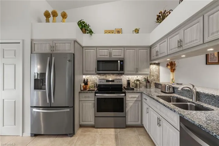 Kitchen featuring stone countertops, tasteful backsplash, stainless steel appliances, sink, and vaulted ceiling