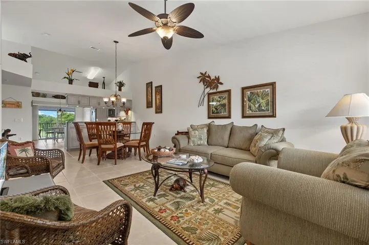 Tiled living room featuring ceiling fan with notable chandelier and high vaulted ceiling