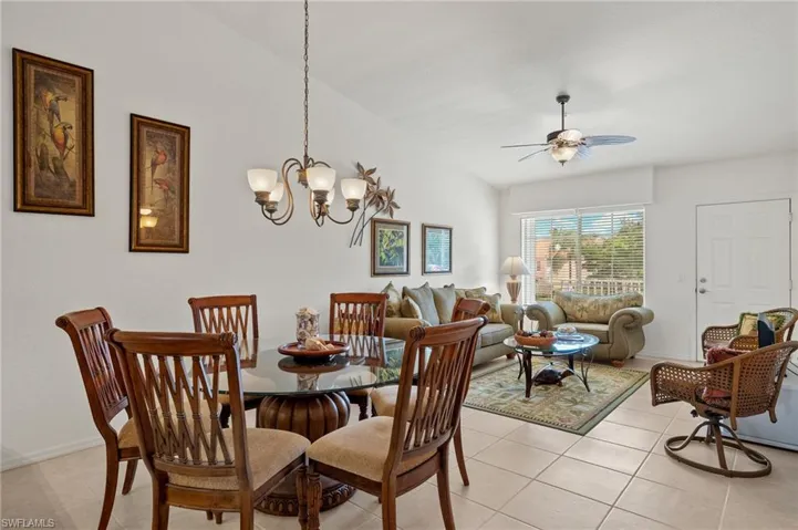 Dining room with light tile patterned floors, vaulted ceiling, and ceiling fan with notable chandelier