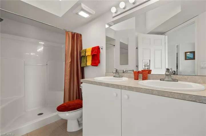 Bathroom with vanity, toilet, walk in shower, and tile patterned flooring