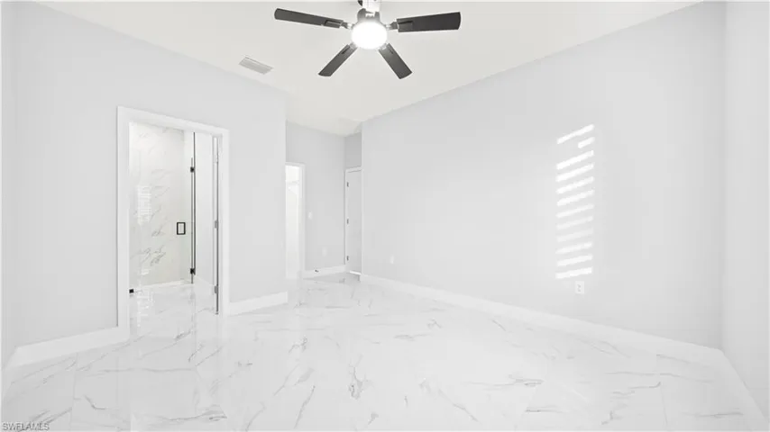 Unfurnished bedroom featuring light marble finish floors, ceiling fan, and ensuite bathroom