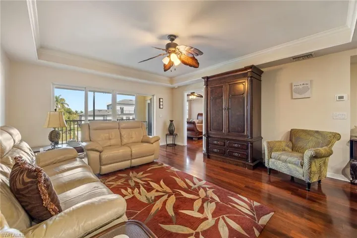 Living room with a raised ceiling, ornamental molding, ceiling fan, and dark wood-type flooring