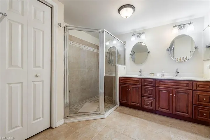 Primary Full bath featuring double vanity, a shower stall, light tile patterned floors, and a closet