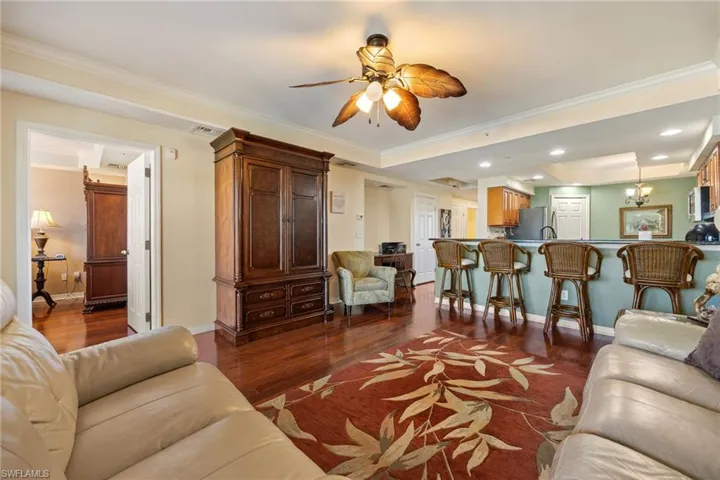 Living area featuring crown molding, a tray ceiling, dark wood-type flooring, a ceiling fan, and recessed lighting