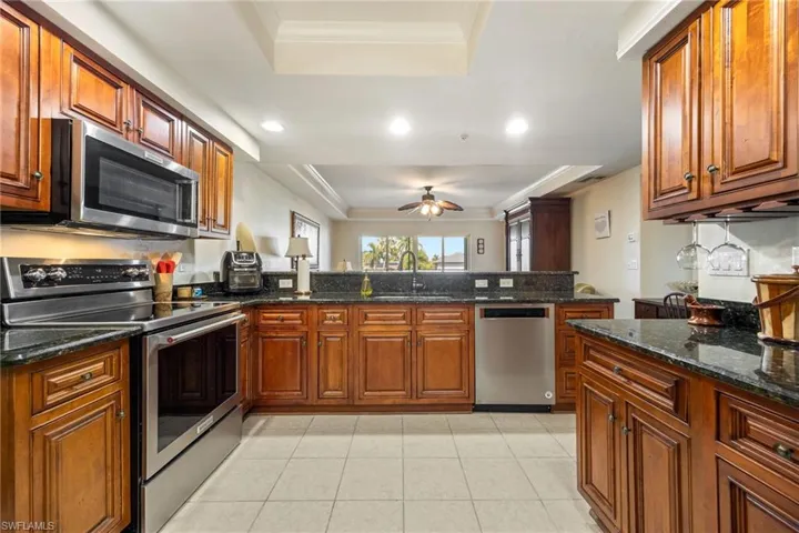 Kitchen featuring a tray ceiling, stainless steel appliances, ornamental molding, dark stone counters, and wood finish cabinets