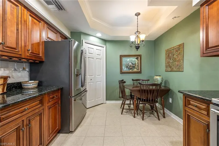 Kitchen featuring dark stone countertops, wood finish cabinetry, crown molding, suspended lighting, and a raised ceiling