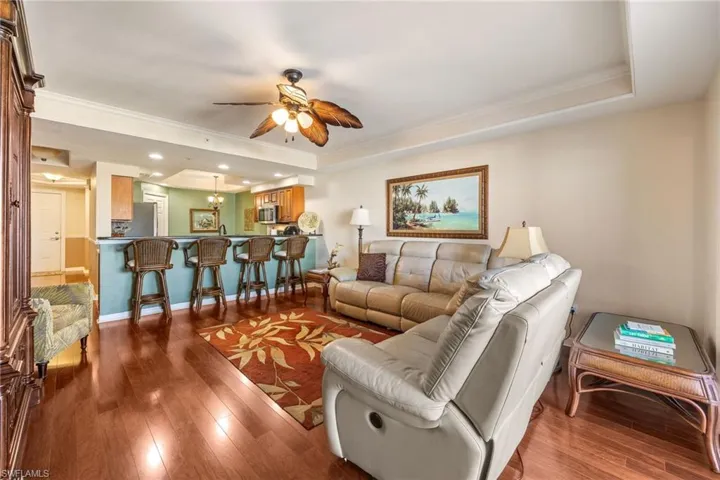 Living area featuring ornamental molding, dark wood-type flooring, a raised ceiling, ceiling fan, and recessed lighting