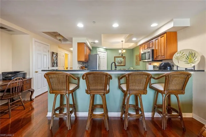 Kitchen featuring wood finish cabinetry, a raised ceiling, a kitchen breakfast bar, dark wood finished floors, and stainless steel appliances