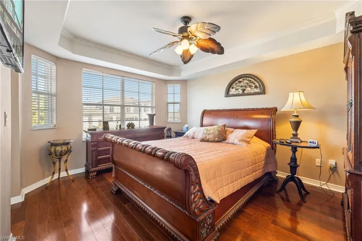 Primary Bedroom with dark wood finished floors, ornamental molding, ceiling fan, and a tray ceiling