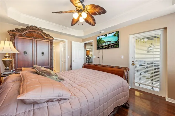 Primary Bedroom featuring access to outside, dark wood finished floors, a raised ceiling, ornamental molding, and a ceiling fan