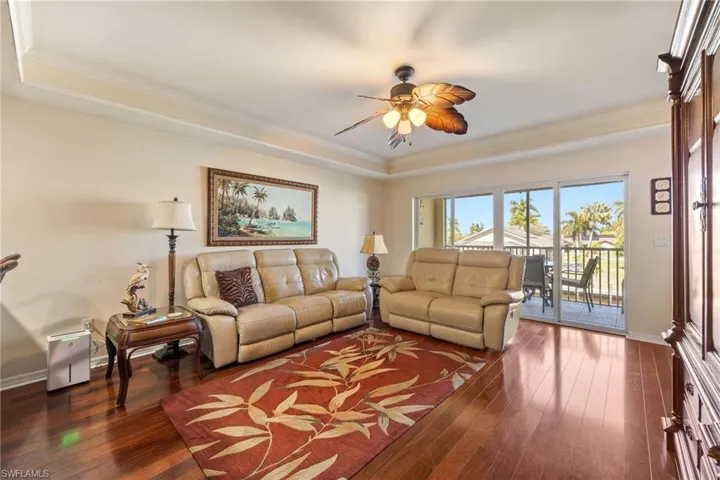 Living room featuring a ceiling fan, ornamental molding, dark wood finished floors, and a tray ceiling