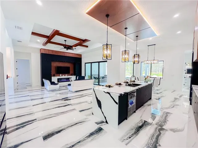 Kitchen with ceiling fan with notable chandelier, an island with sink, pendant lighting, coffered ceiling, and light tile floors