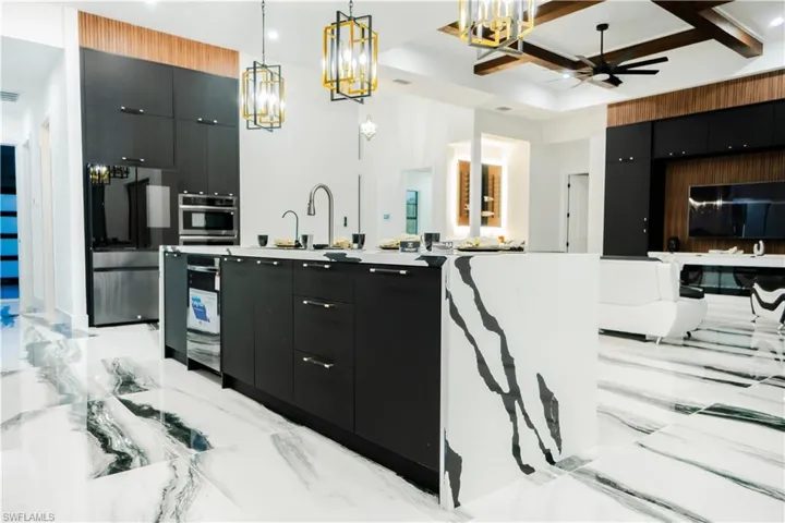 Kitchen featuring ceiling fan with notable chandelier, appliances with stainless steel finishes, decorative light fixtures, coffered ceiling, and light tile floors