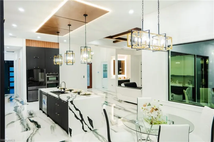 Kitchen with an island with sink, light tile floors, hanging light fixtures, sink, and stainless steel double oven
