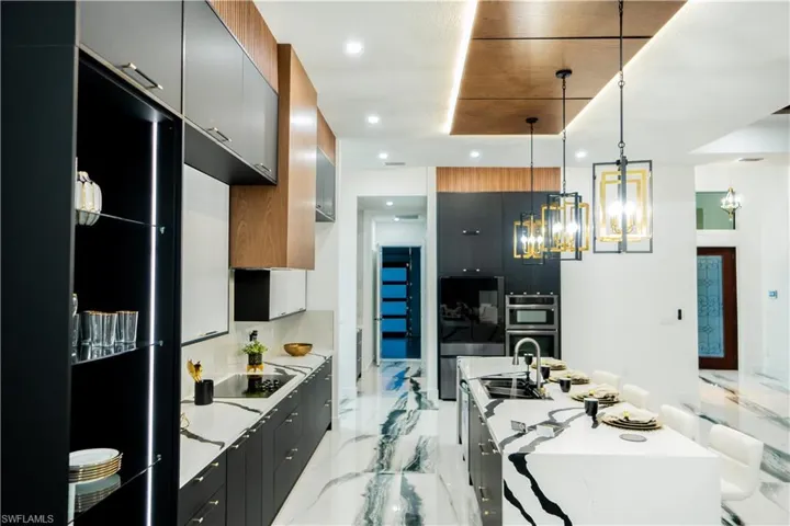 Kitchen featuring light tile flooring, black appliances, hanging light fixtures, sink, and a kitchen island with sink