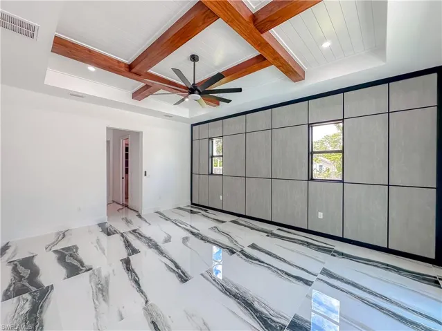 Tiled spare room with coffered ceiling, beam ceiling, a tray ceiling, and ceiling fan