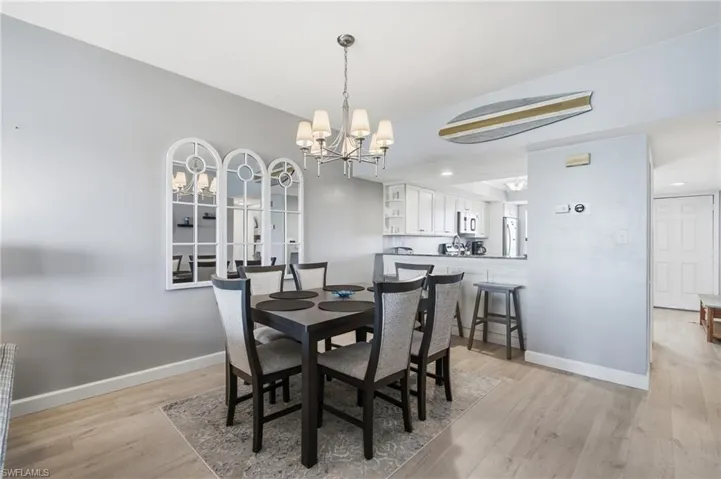 Dining area with wood-finish flooring, a contemporary chandelier, and a decorative mirror triptych - Virtually Edited Image