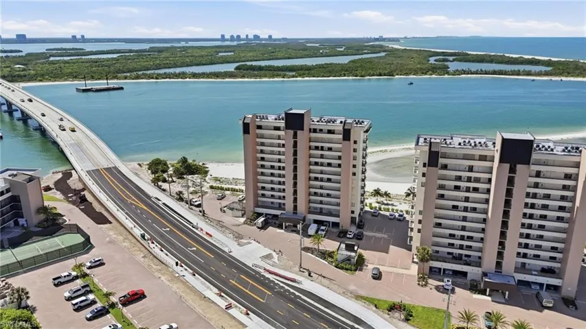 Waterfront high-rise building featuring multiple balconies, direct access to a sandy shoreline, and proximity to a bridge - Virtually Edited Image