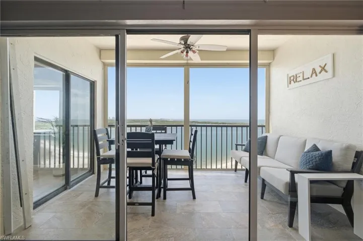 Expansive screened balcony featuring a ceiling fan, tiled flooring, and panoramic water and coastline views - Virtually Edited Image