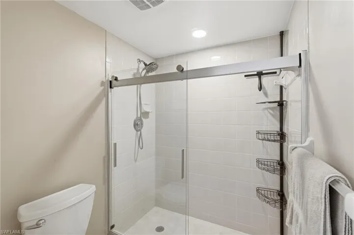Glass-enclosed shower featuring white subway tile surround, a rain shower head, and a handheld sprayer - Virtually Edited Image