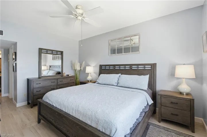Bedroom featuring light wood-finish flooring, a white ceiling fan with integrated lighting, and light gray wall paint - Virtually Edited Image