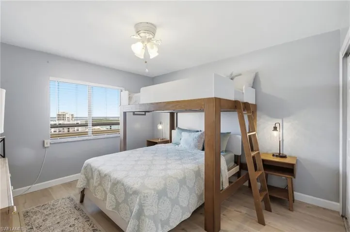 Light-filled bedroom featuring a wood-finish bunk bed, pale wood-finish flooring, and a ceiling fan with light fixture - Virtually Edited Image