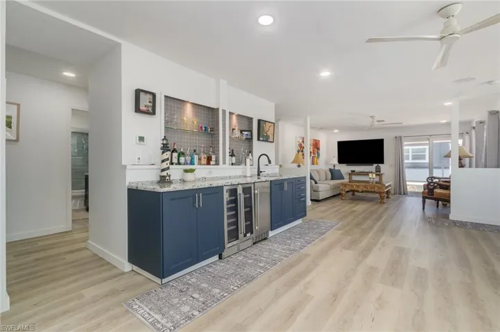 Indoor wet bar with light stone countertops, blue cabinets, light wood-style floors, recessed lighting, and beverage cooler