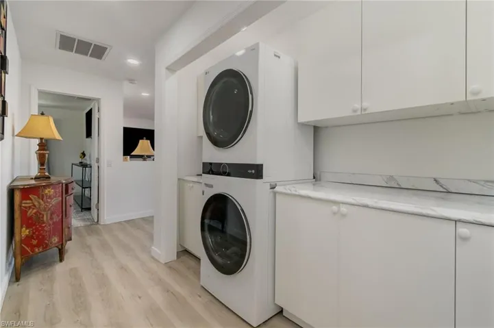 Washroom with stacked washer / dryer, light wood-style flooring, recessed lighting, and cabinet space